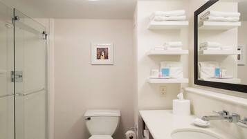 Un baño moderno con cabina de ducha de vidrio, inodoro, lavabo con espejo y repisas con toallas.
