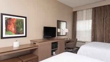A hotel room with a bed, a desk with a television, a mirror, a lamp, and a picture on the wall.