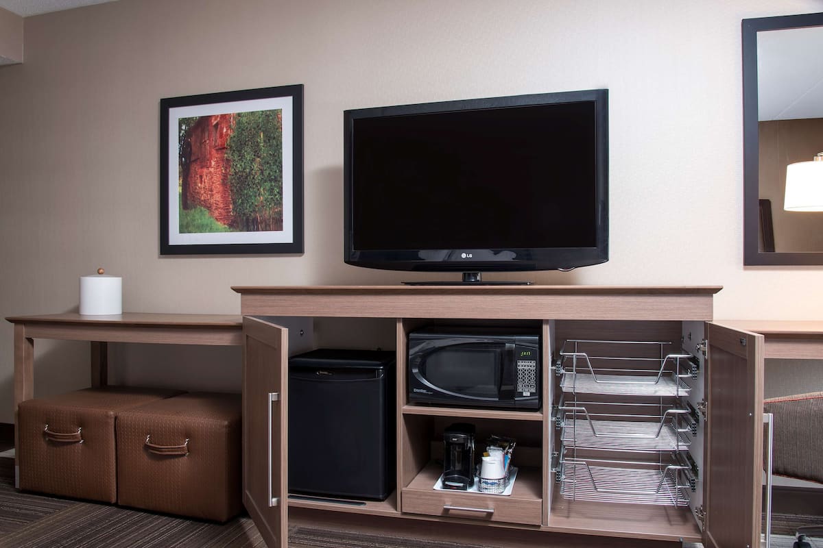 A hotel room with a flat-screen TV, a framed picture on the wall, a small refrigerator, a microwave, and a coffee maker.