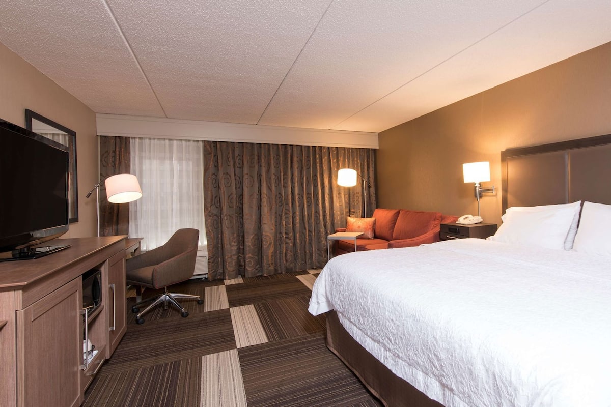 A hotel room with a bed, a desk with a TV, a chair, a sofa, and two bedside lamps.