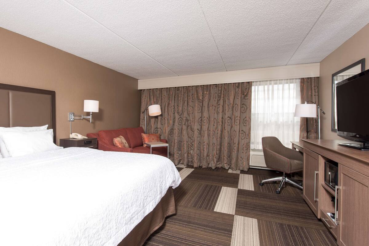 A hotel room with a bed, a desk, a television, a chair, and a window with curtains.