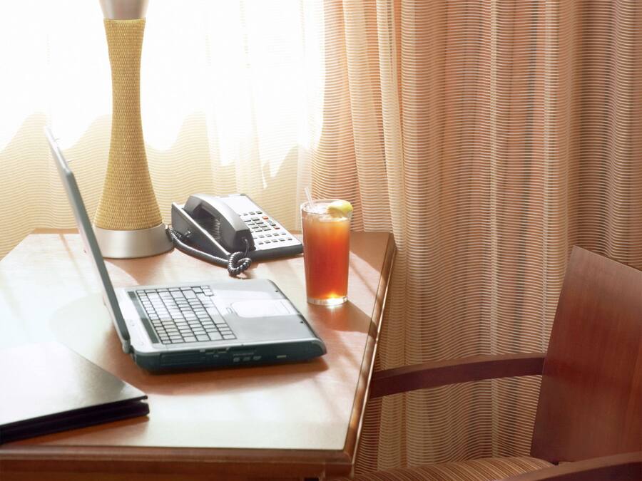 A wooden table with a laptop, a telephone, and a glass of iced tea.