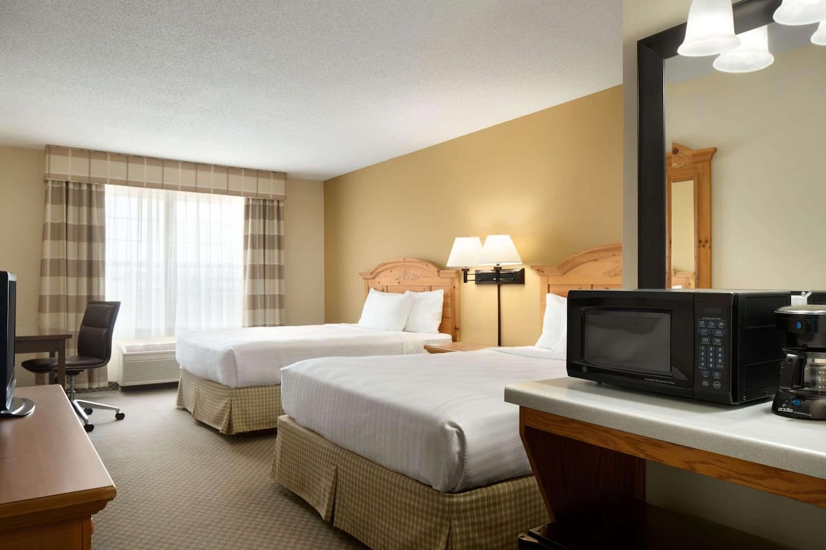 A hotel room with two beds, a desk, a chair, a microwave, and a coffee maker.