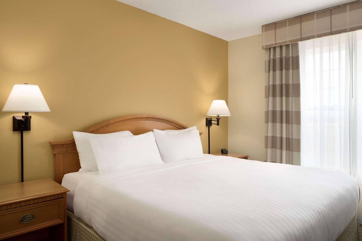 A hotel room with a large bed, two bedside tables with lamps, a wooden headboard, and a window with curtains.