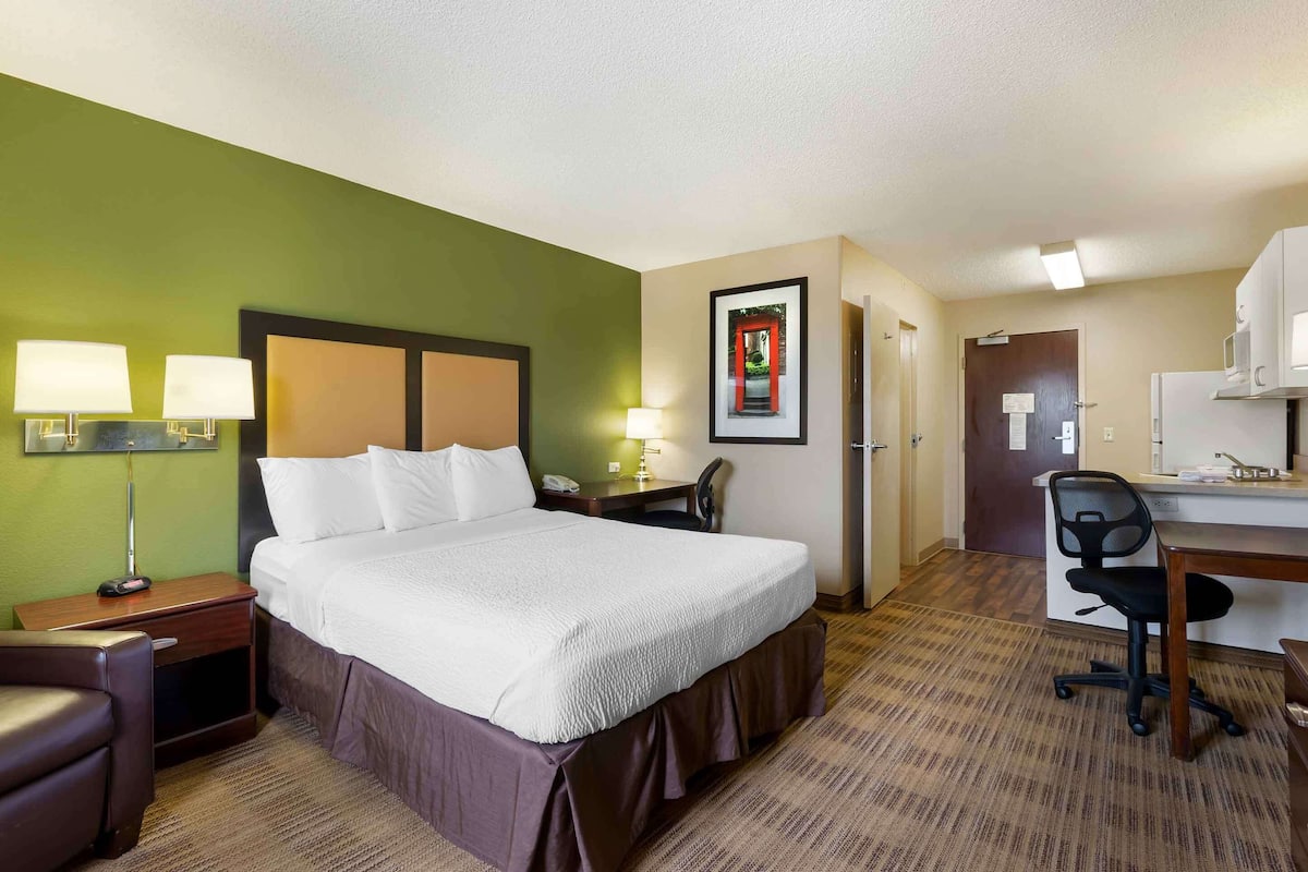Une chambre d’hôtel avec un lit, un bureau, une chaise et un tableau encadré au mur.