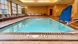 Piscina interna com borda em azulejo, cadeiras de descanso e um banco coberto.