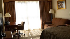 Quarto de hotel com cama, escrivaninha com computador, cadeira, sofá e abajur.