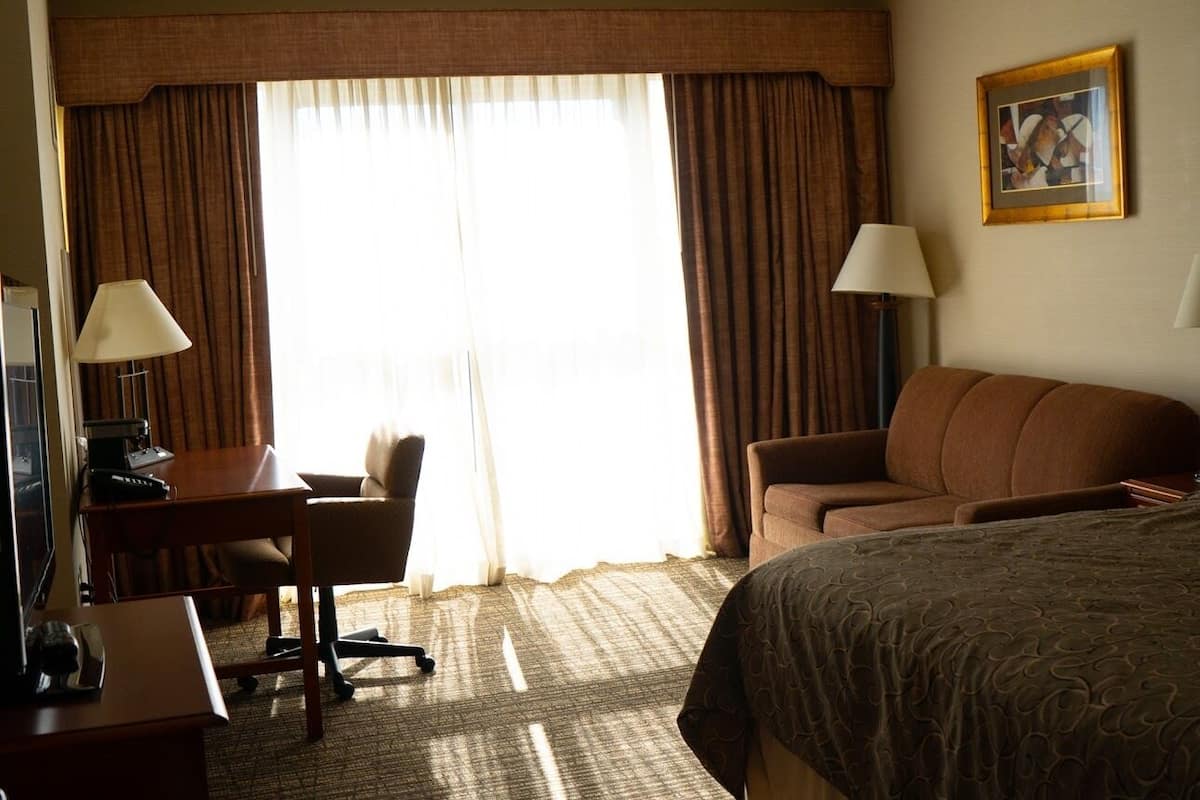 Una habitación de hotel con cama, escritorio con computadora, silla, sofá y lámpara.