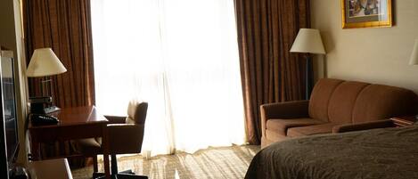 A hotel room with a bed, a desk with a computer, a chair, a sofa, and a lamp.