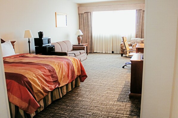 A hotel room with a large bed, a desk, a chair, a sofa, and a window with curtains.