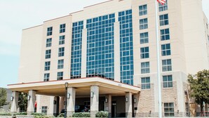 Um hotel de vários andares com uma bandeira americana em destaque, janelas amplas e uma área de entrada coberta.