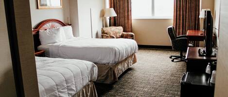 A hotel room with two beds, a desk, a chair, a television, and a window with curtains.