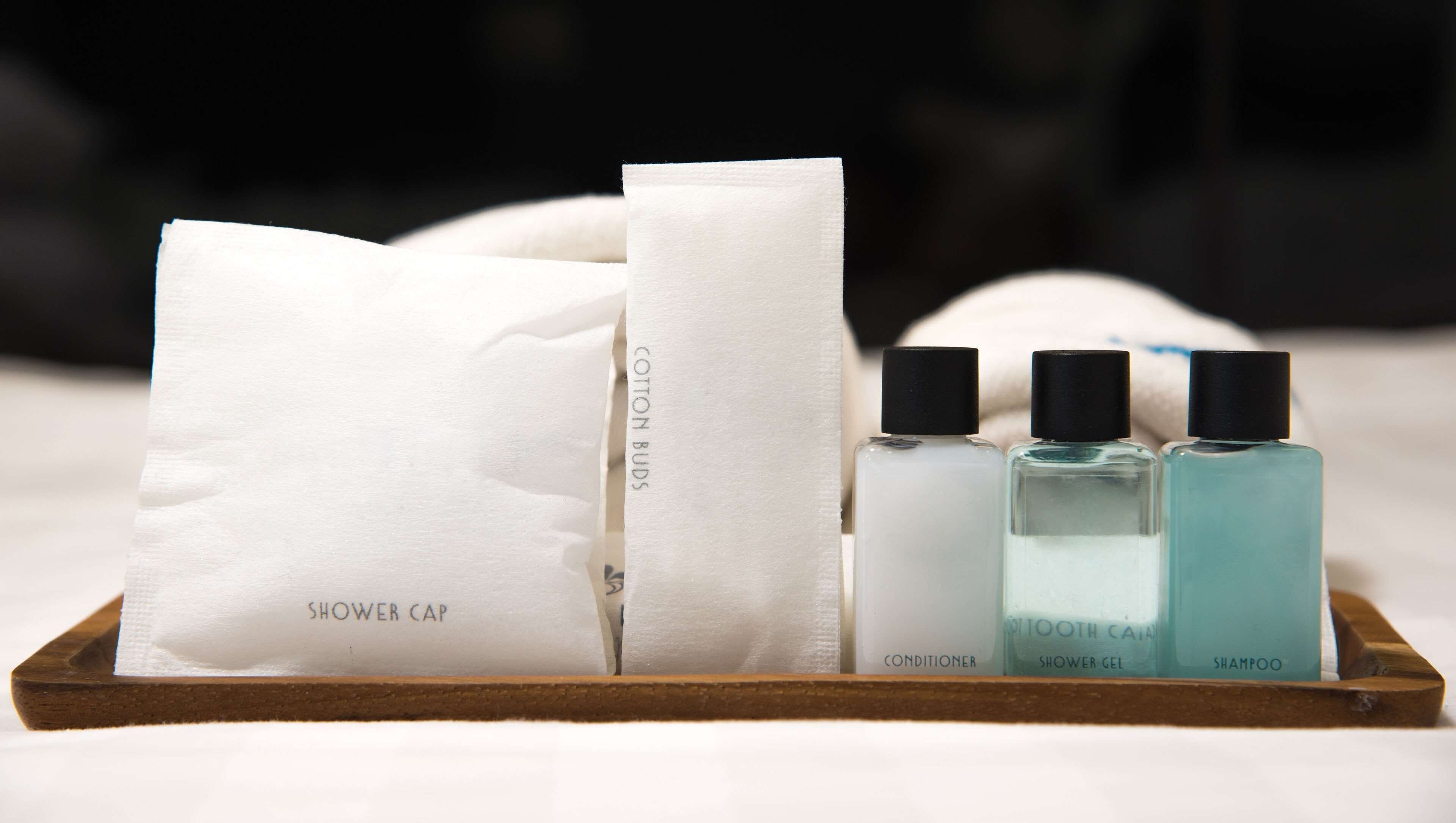 A wooden tray with a white shower cap, a white cotton bud, a conditioner bottle, a toothbrush, and a shampoo bottle.