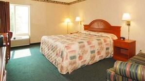 A hotel room with a bed, two bedside lamps, a wooden nightstand, a chair, and a window with curtains.
