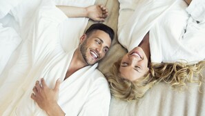 A couple lying in bed, covered with white blankets.