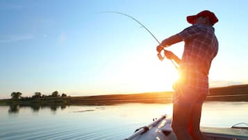 Una persona pescando en un bote con un lago tranquilo y una puesta de sol al fondo.