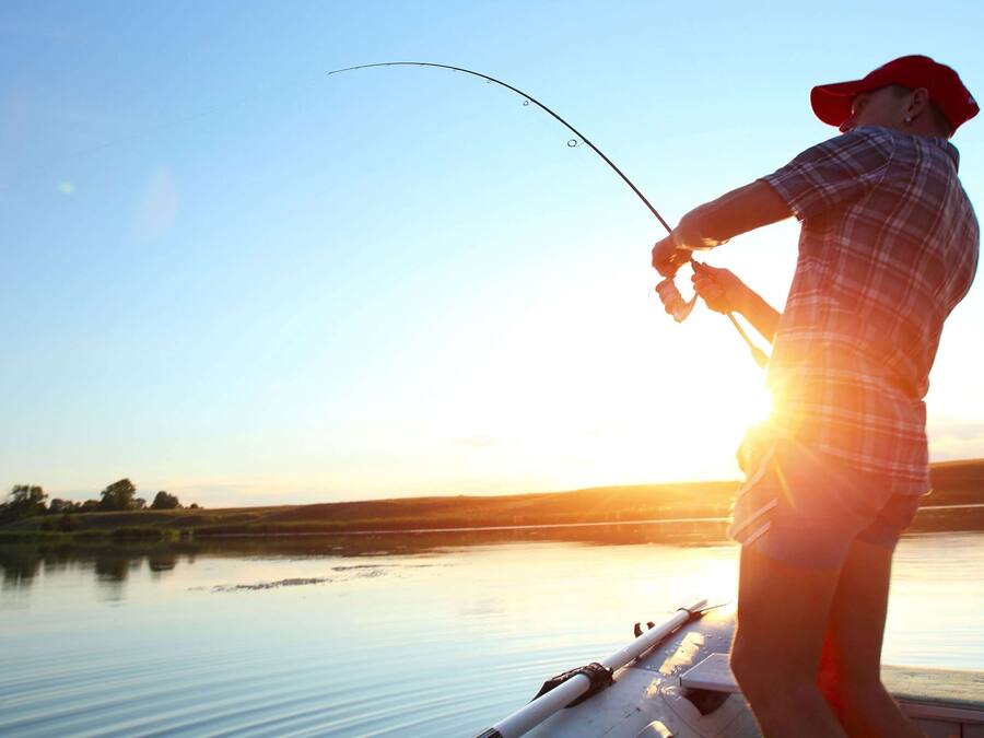 Una persona pescando en un bote con un lago tranquilo y una puesta de sol al fondo.