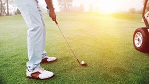 A person preparing to put a golf ball on a green, with a golf cart nearby. - Beaver Dam Inn (Beaver Dam)