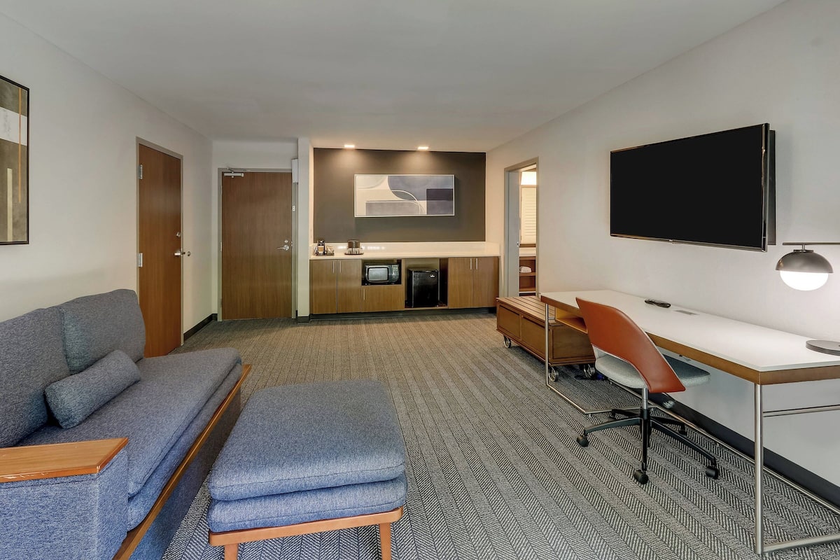 Habitación de hotel con sofá, escritorio, televisión y kitchenette.