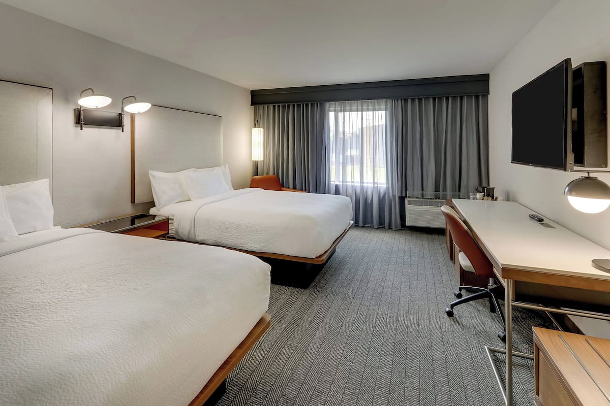 Habitación de hotel con dos camas, un escritorio, una silla, un televisor y una ventana con cortinas.
