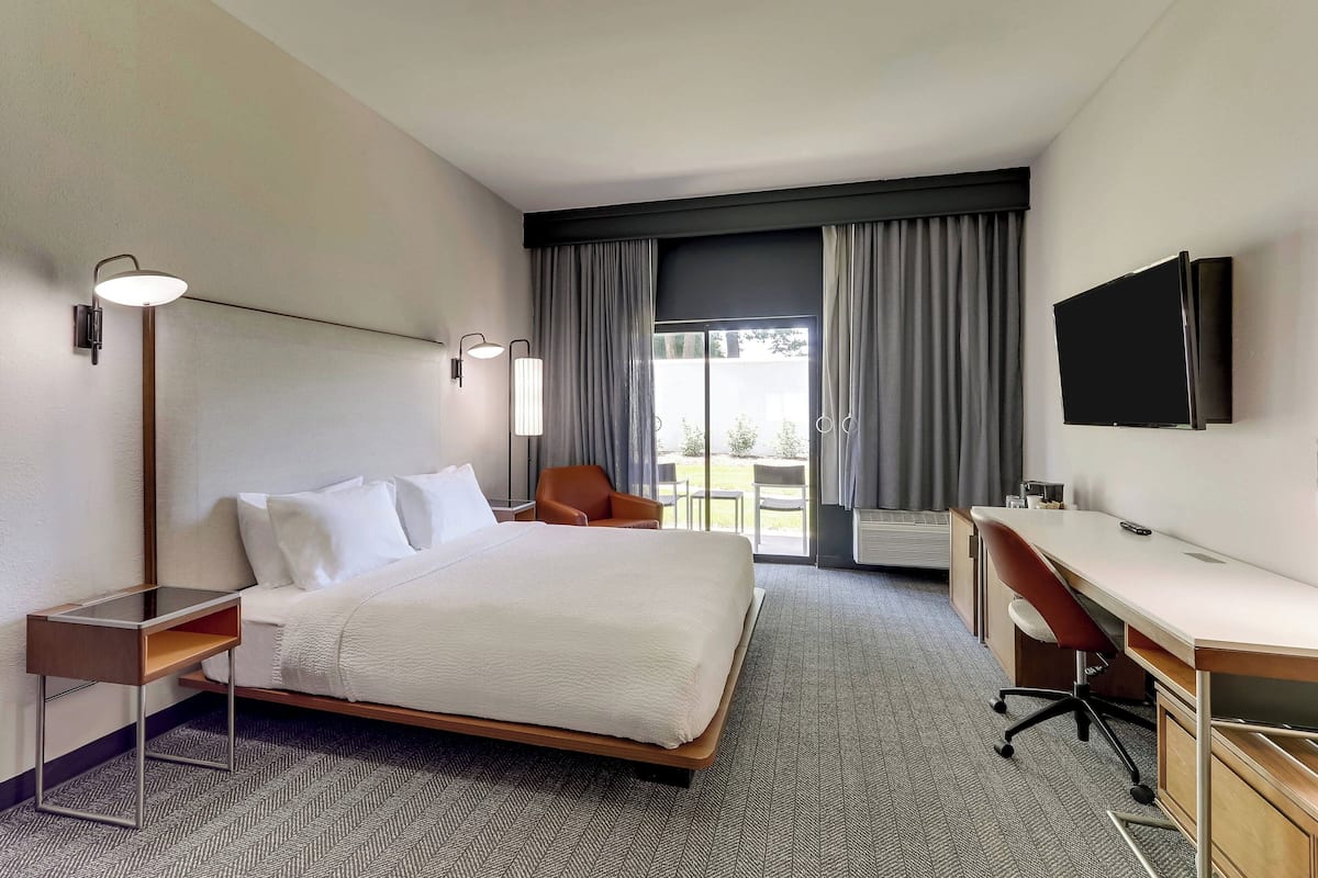 Una habitación de hotel con cama, escritorio, silla, televisor y ventana con cortinas.