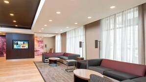A modern hotel lobby with a large seating area, a flat-screen TV, and a large window with sheer curtains. - Courtyard by Marriott Louisville Downtown (Louisville)