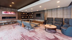 A modern living room with a fireplace, comfortable seating, and a large TV. - Courtyard by Marriott Louisville Downtown (Louisville)