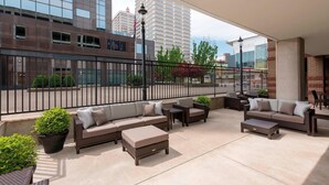 An outdoor patio area with wicker furniture, including sofas and a coffee table, surrounded by a black metal fence. - Courtyard by Marriott Louisville Downtown (Louisville)