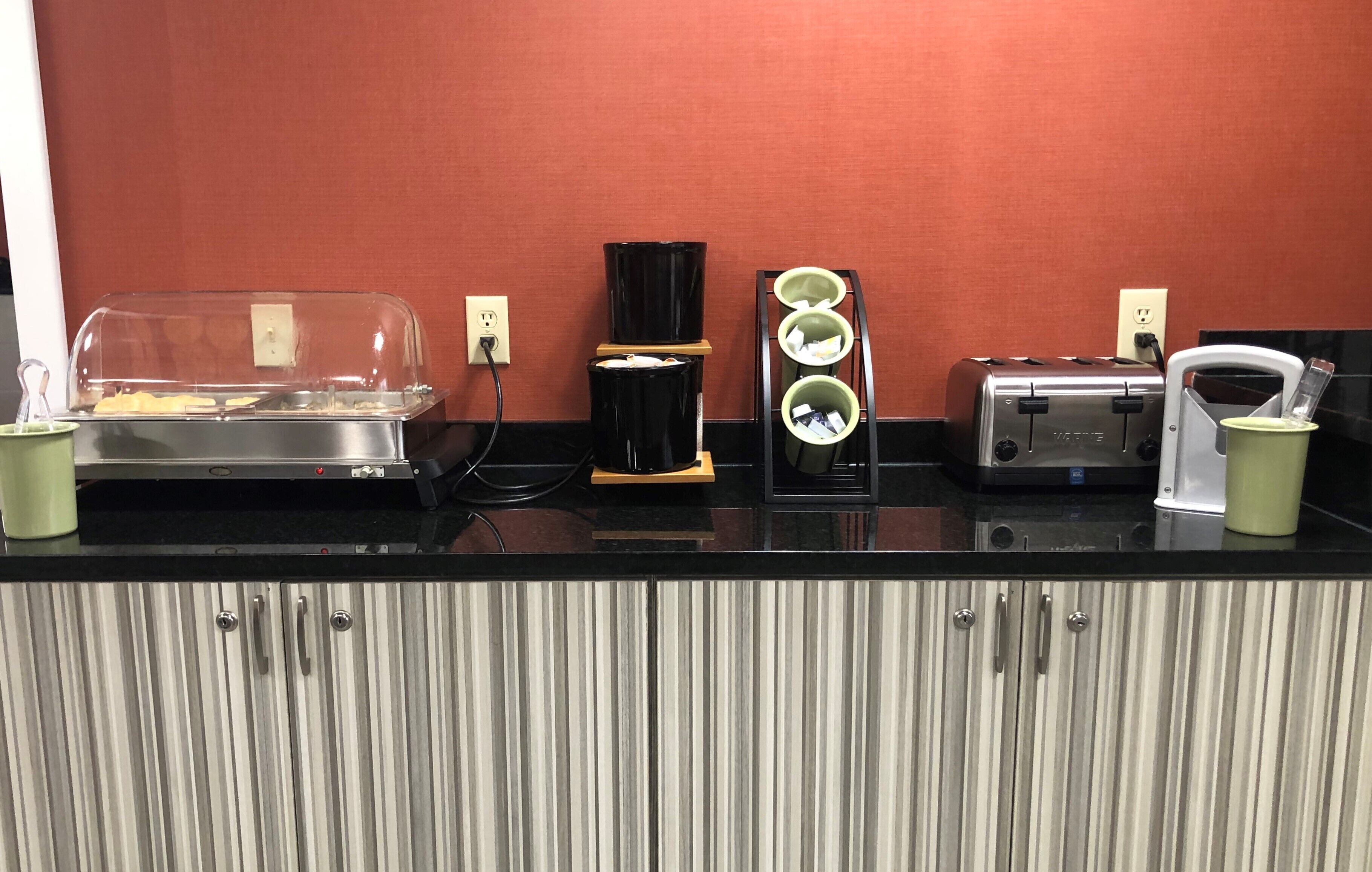 A kitchenette with a toaster, a coffee maker, and a food warmer.