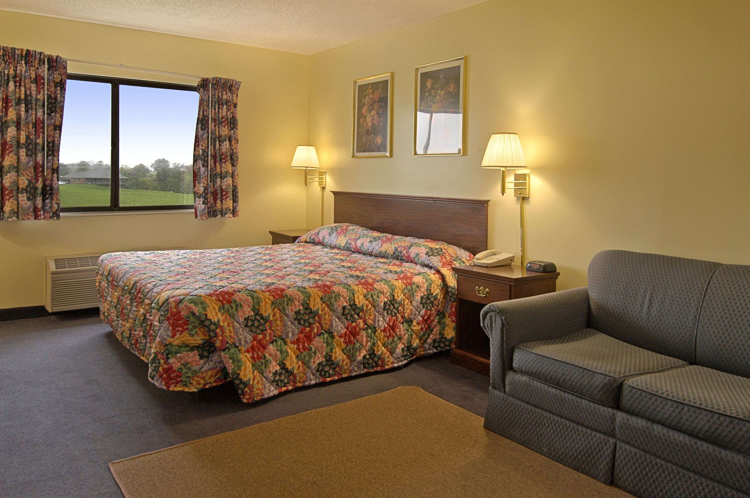 Una habitación de hotel con cama, sofá, dos lámparas, una mesita de noche y una ventana con cortinas.