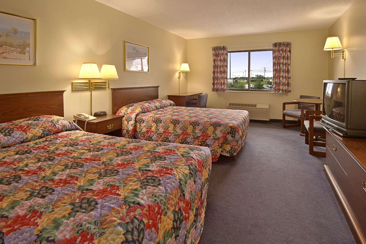 A hotel room with two beds, a desk, a television, and a window with curtains.