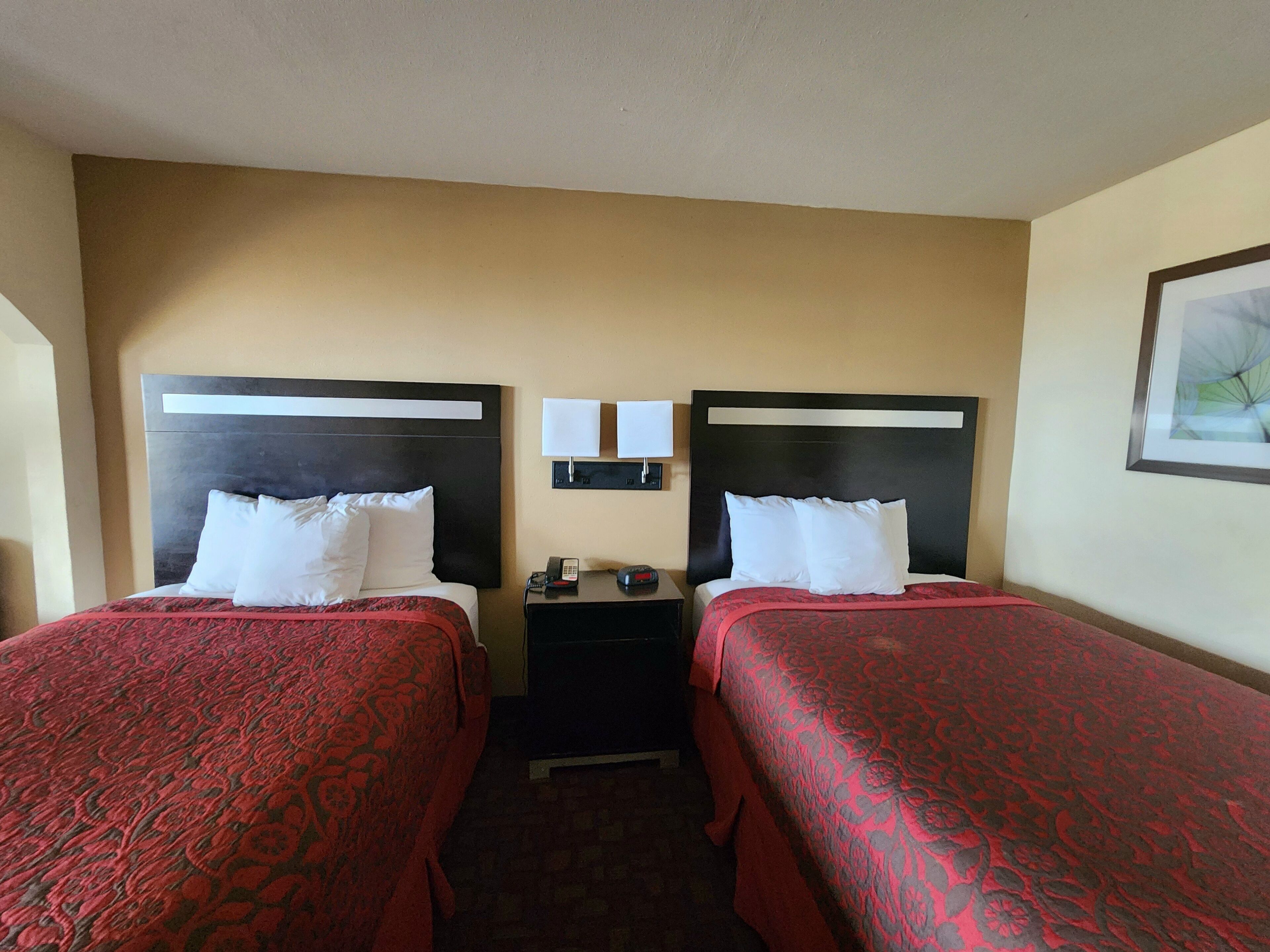 A hotel room with two beds, each with a headboard, a nightstand with a phone and a lamp, and a framed picture on the wall.