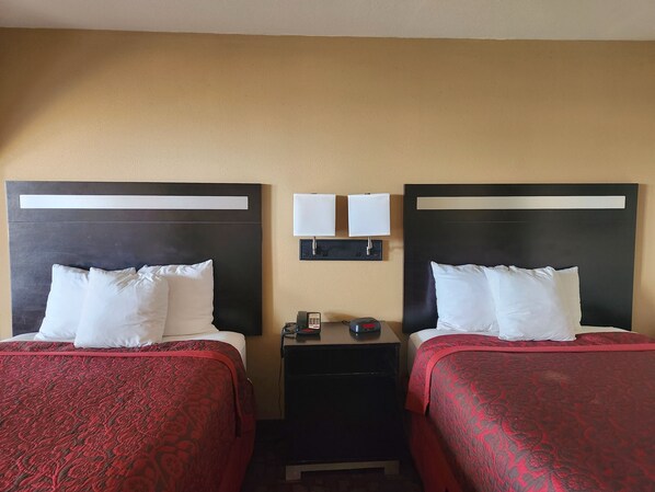 A hotel room with two beds, each with a red bedspread and white pillows. There are two bedside tables with lamps and a phone. The walls are beige, and there is a flat-screen TV mounted above the beds. - Days Inn by Wyndham Hammond (Hammond)