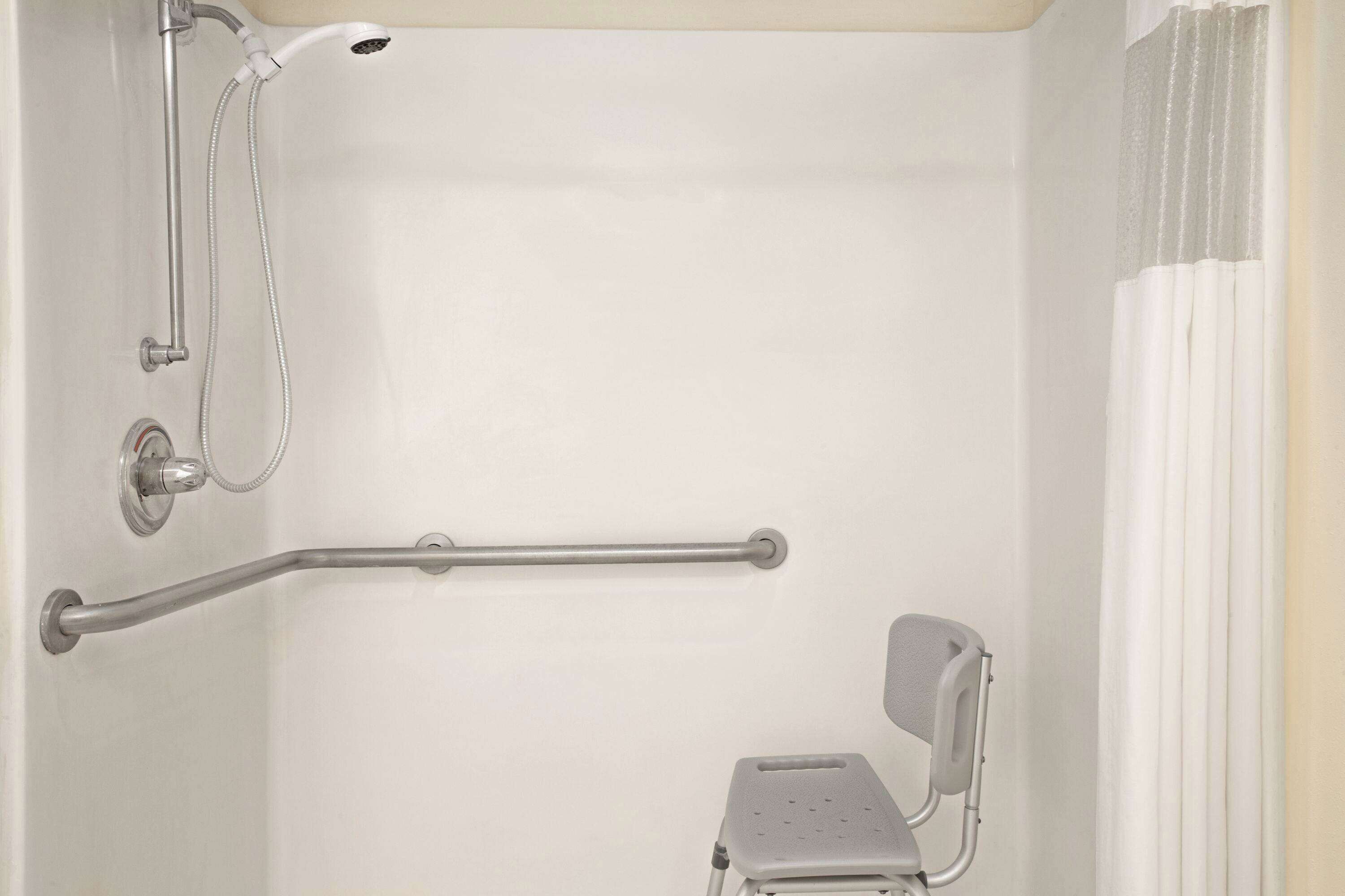 Une salle de bain équipée d’une douche, de barres d’appui et d’un marchepied.