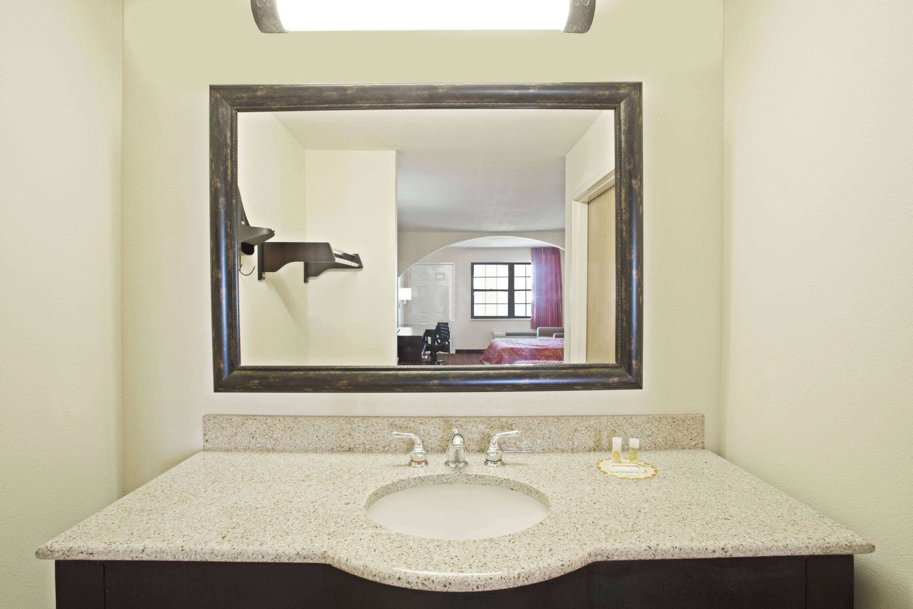 Un baño con encimera de granito, lavamanos y espejo.