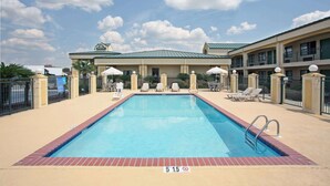 A swimming pool with lounge chairs and umbrellas, a covered seating area, and a building with a green roof. - Days Inn by Wyndham Hammond (Hammond)