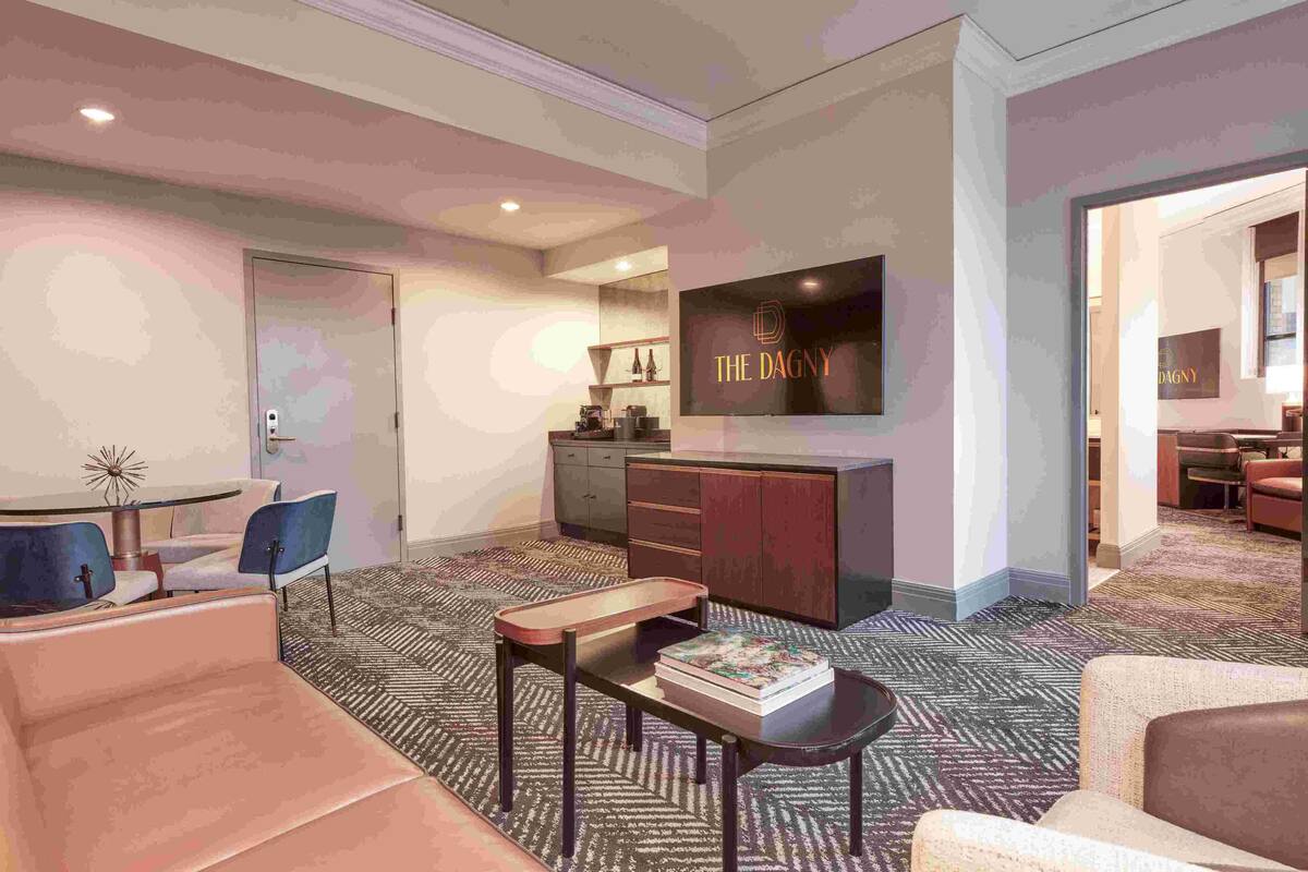 Habitación de hotel moderna con comedor, televisor montado en la pared y suelo alfombrado.