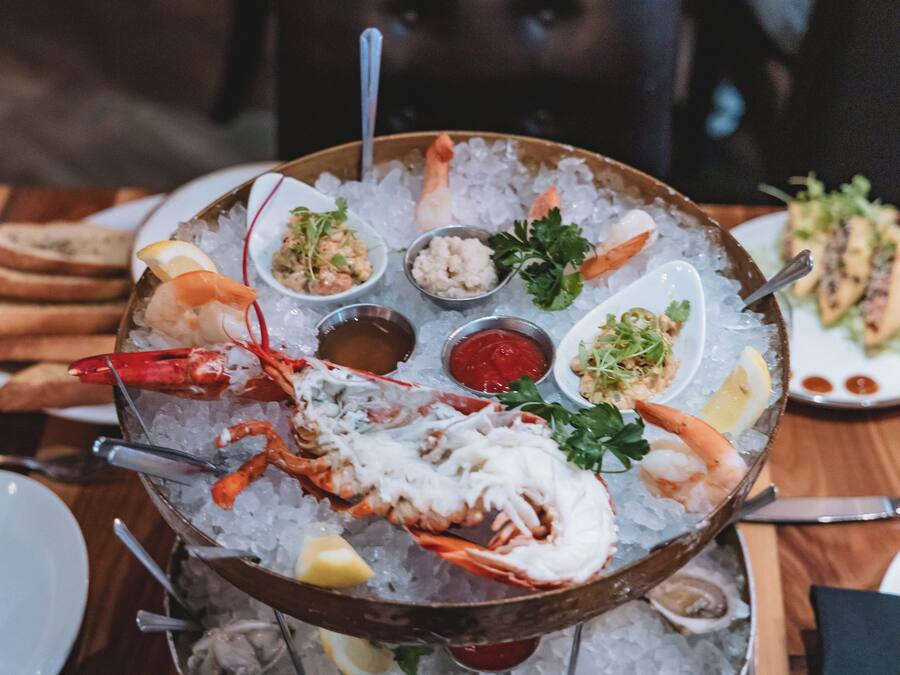 A seafood platter on ice with various dishes, including shrimp, lobster, and other seafood, accompanied by lemon wedges and garnishes.