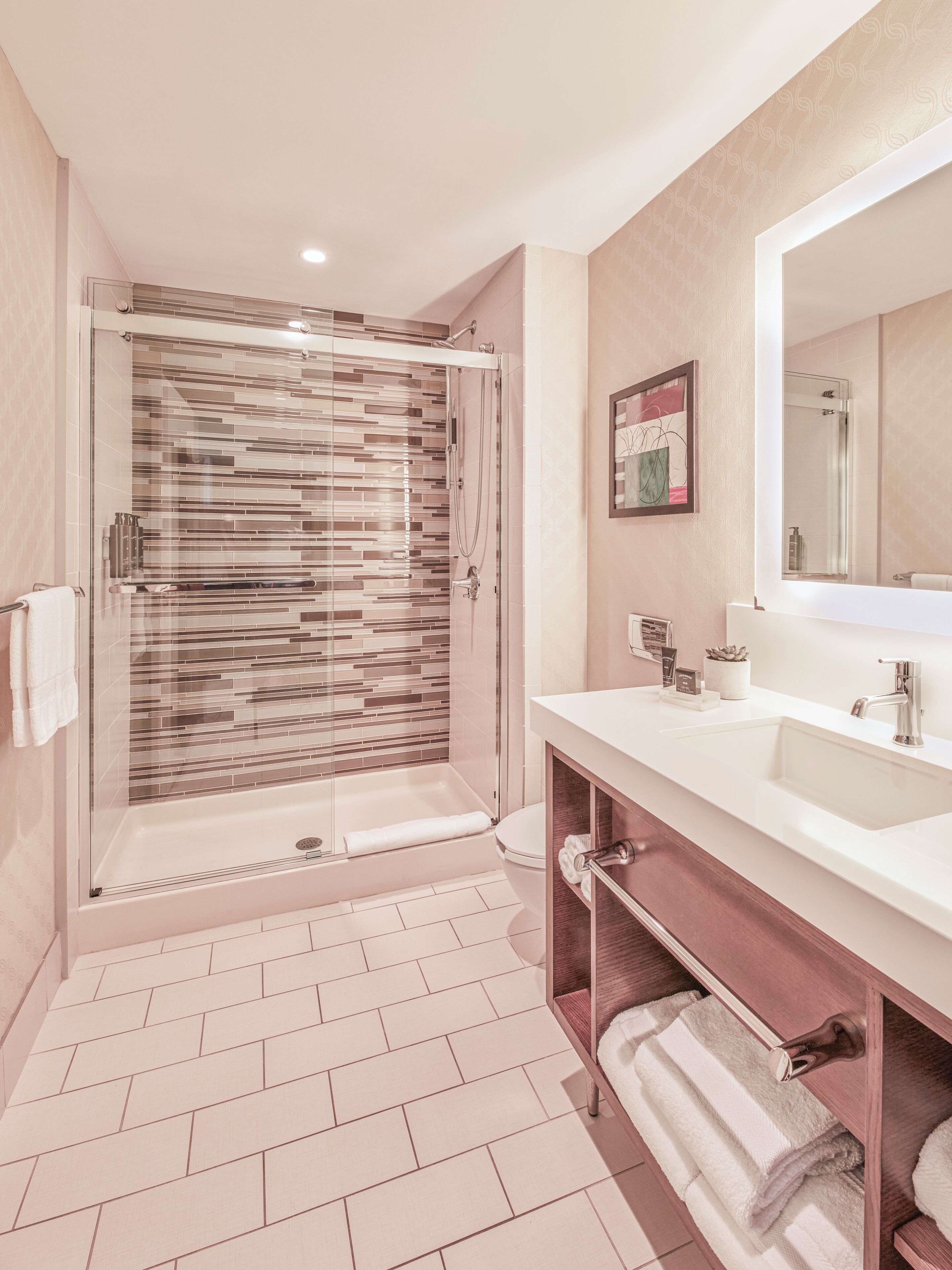 Un baño moderno con ducha de vidrio, lavamanos blanco y un espejo grande.