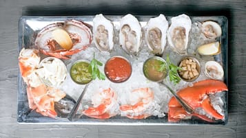 A seafood platter with various types of shellfish and shrimp on ice, accompanied by two types of sauces and lemon wedges.