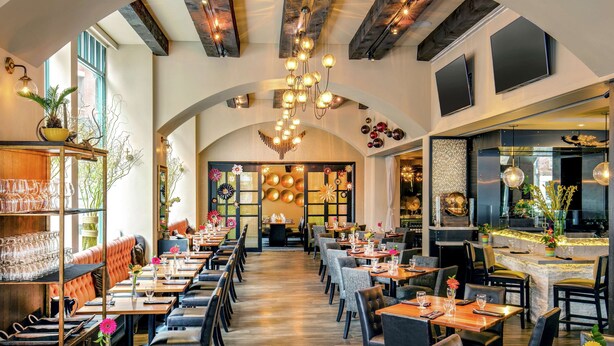 Un restaurante con un amplio comedor, techos altos y vigas a la vista. Las mesas están preparadas con cristalería y centros de mesa.