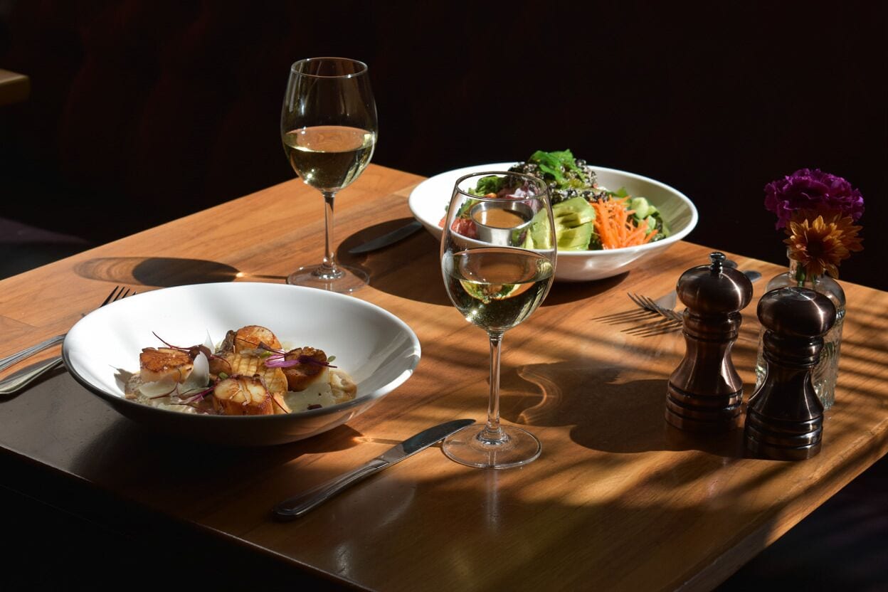 Una mesa de madera con dos cuencos de comida, dos copas de vino y saleros y pimenteros.