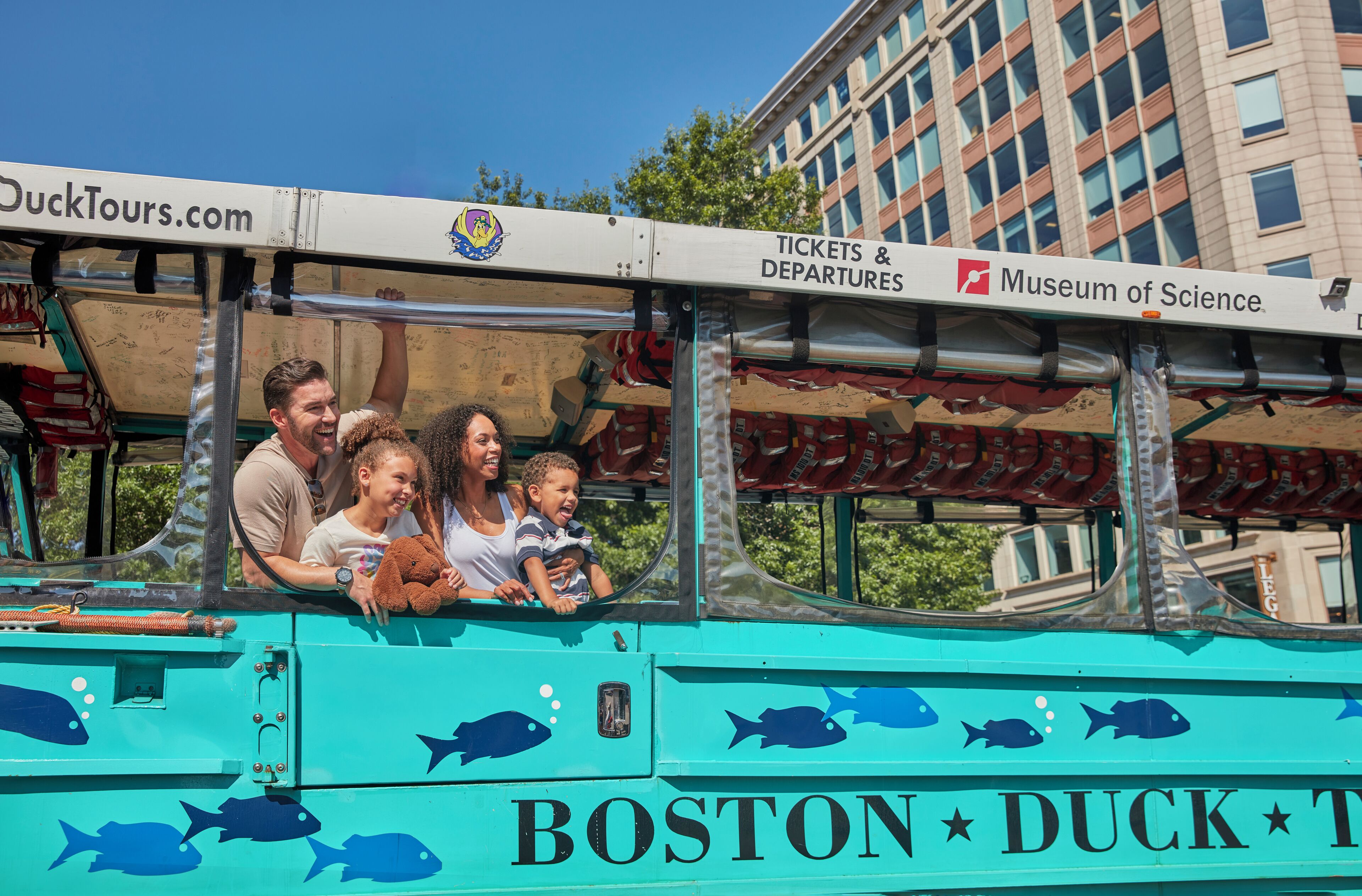 A teal bus with fish decals and the text "BOSTON DUCK TOUR" and "Tickets & Departures Museum of Science."