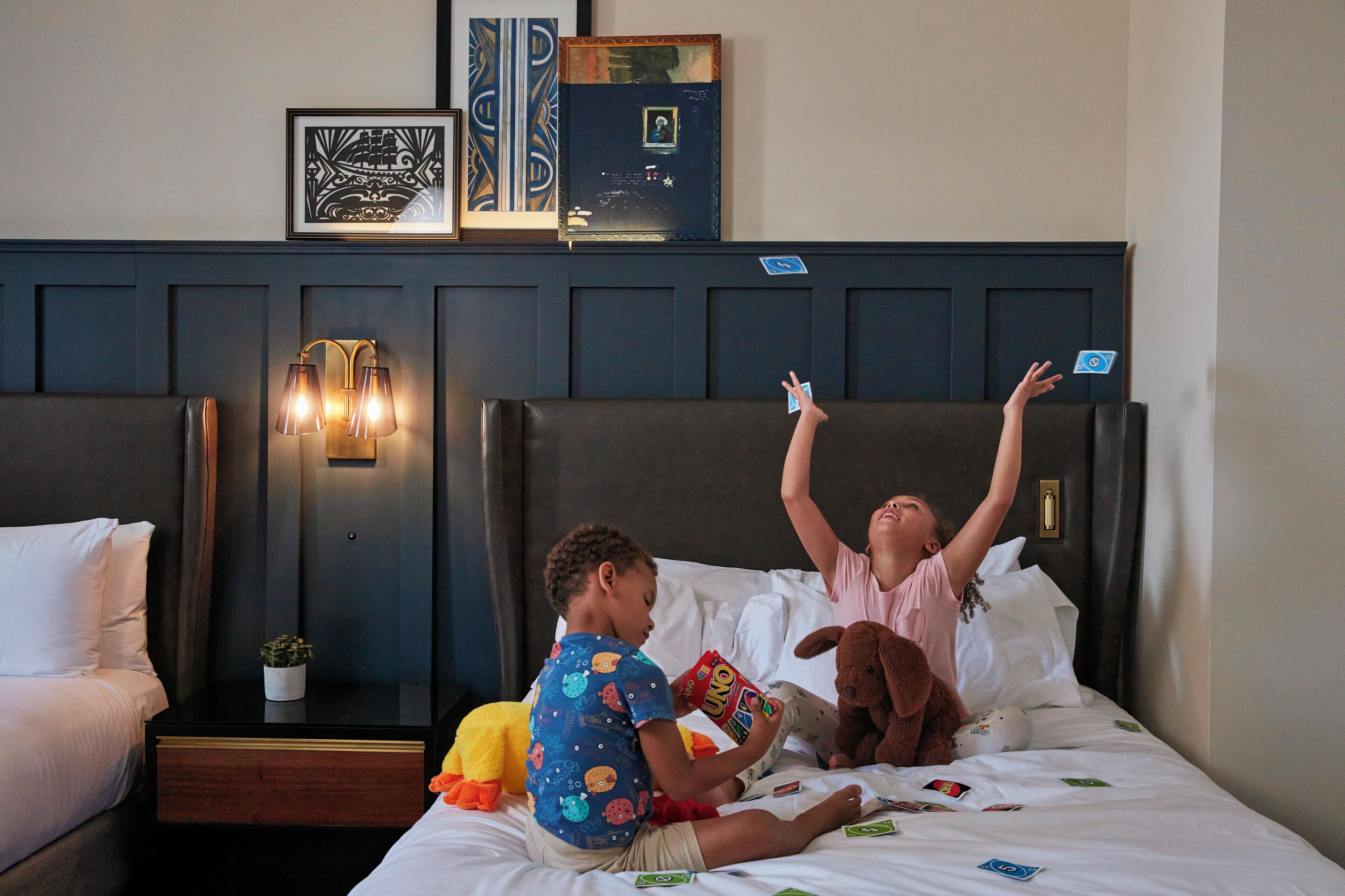Ein Hotelzimmer mit einem Bett, einem Nachttisch mit Lampe und gerahmten Bildern an der Wand.