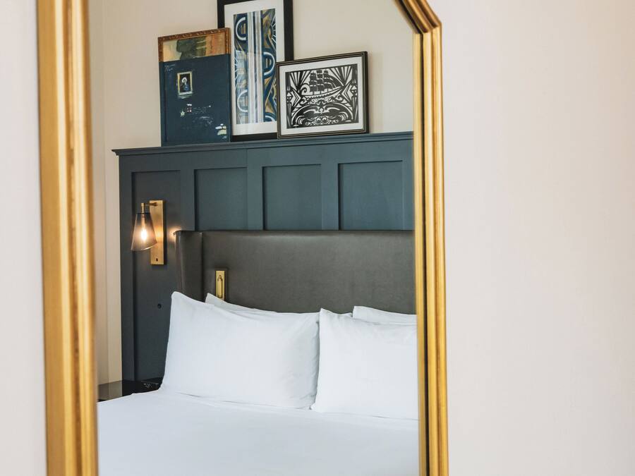 A neatly made bed with white linens, a dark headboard, and a wall-mounted light fixture.