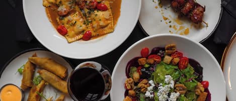 Una mesa con diversos platos, incluyendo ravioles, brochetas, rollitos primavera y una ensalada.