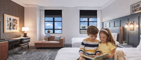 A hotel room with a large bed, a desk, a sofa, and two windows.