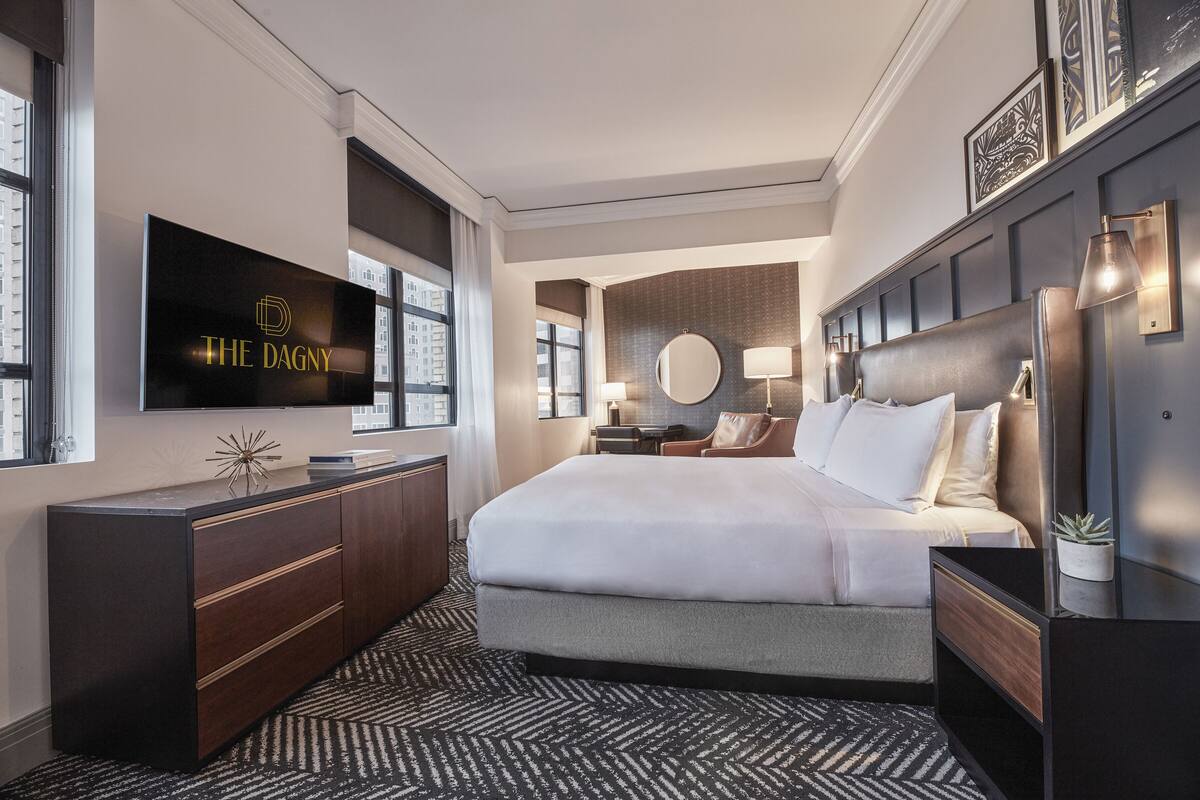 Una habitación de hotel moderna con una cama grande, un televisor de pantalla plana, un escritorio y vistas a la ciudad.