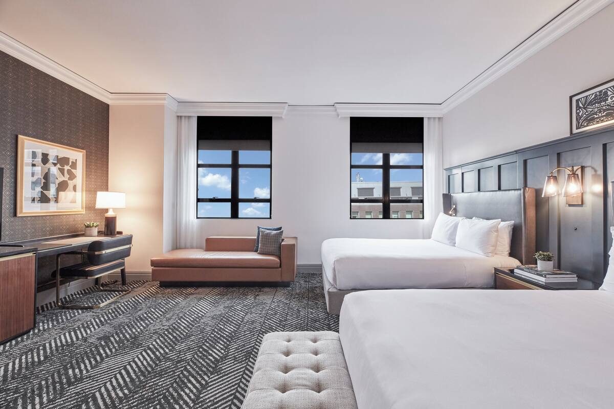 Habitación de hotel con dos camas, un escritorio, un sofá y un ventanal grande.