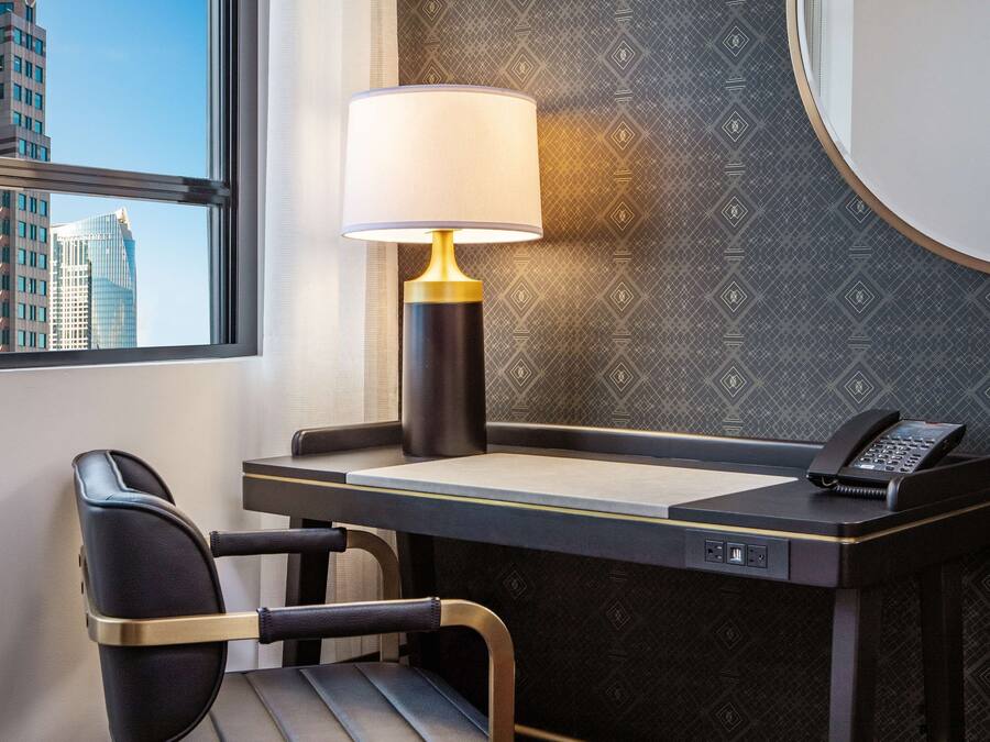 A modern hotel room with a desk, a chair, a lamp, and a phone.